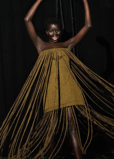 Woman wearing a mustard yellow dress with long fringes against a dark background